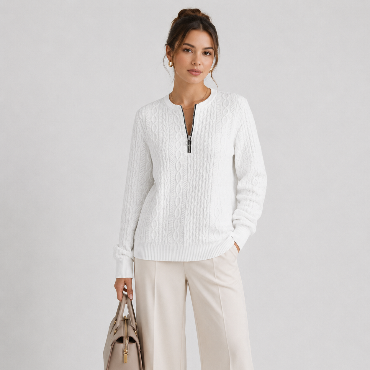 A woman modeling a white textured knit half-zip sweater with a stand collar, paired with light beige wide-leg trousers and holding a taupe handbag, set against a plain light gray studio background.