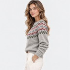 A woman wearing a gray knit sweater with a multicolor Fair Isle pattern across the chest and sleeves, paired with cream pants, photographed against a clean white studio background.