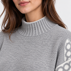 Close-up of a woman wearing a light gray ribbed mock neck sweater with a white geometric pattern on the sleeve, against a light gray background.