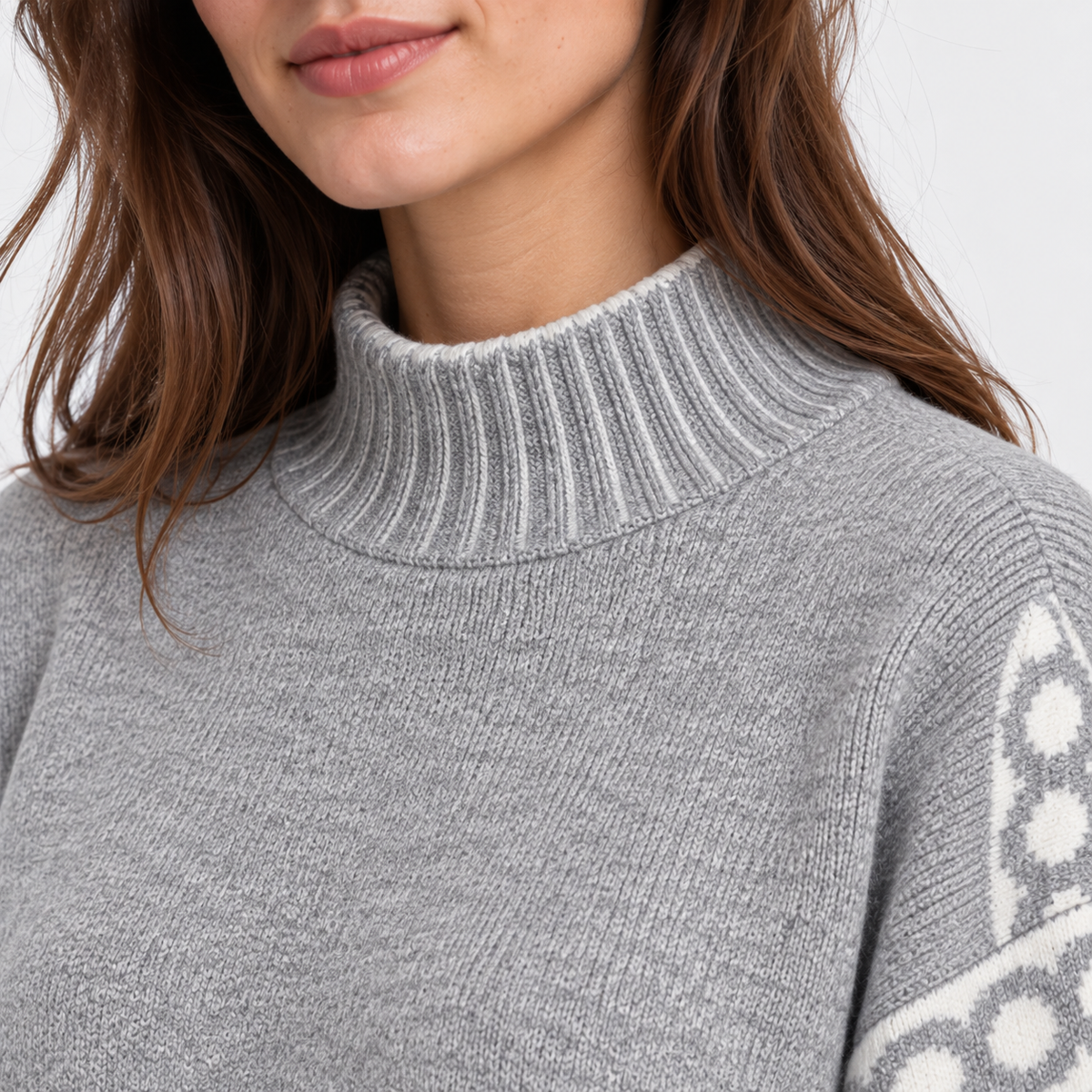 Close-up of a woman wearing a light gray ribbed mock neck sweater with a white geometric pattern on the sleeve, against a light gray background.