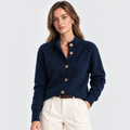 A woman wearing a navy blue knit button-front cardigan with a high ribbed collar, paired with cream trousers and a brown belt, photographed against a clean light gray studio background.