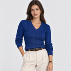 A woman modeling a royal blue cable-knit V-neck sweater, paired with cream-colored trousers and a brown belt, against a light gray studio background.