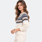 A woman wearing a cream-colored knit sweater with a colorful geometric Fair Isle pattern across the chest in navy, blue, brown, and white, paired with cream pants, against a plain white background.