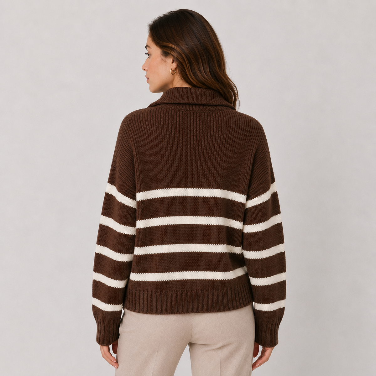 A woman shown from the back wearing a brown ribbed knit sweater with horizontal cream stripes across the body and sleeves, paired with light beige pants, against a light gray studio background.