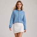 A woman modeling a blue and white striped cropped button-up cardigan sweater paired with a white mini skirt, set against a plain light gray studio background.