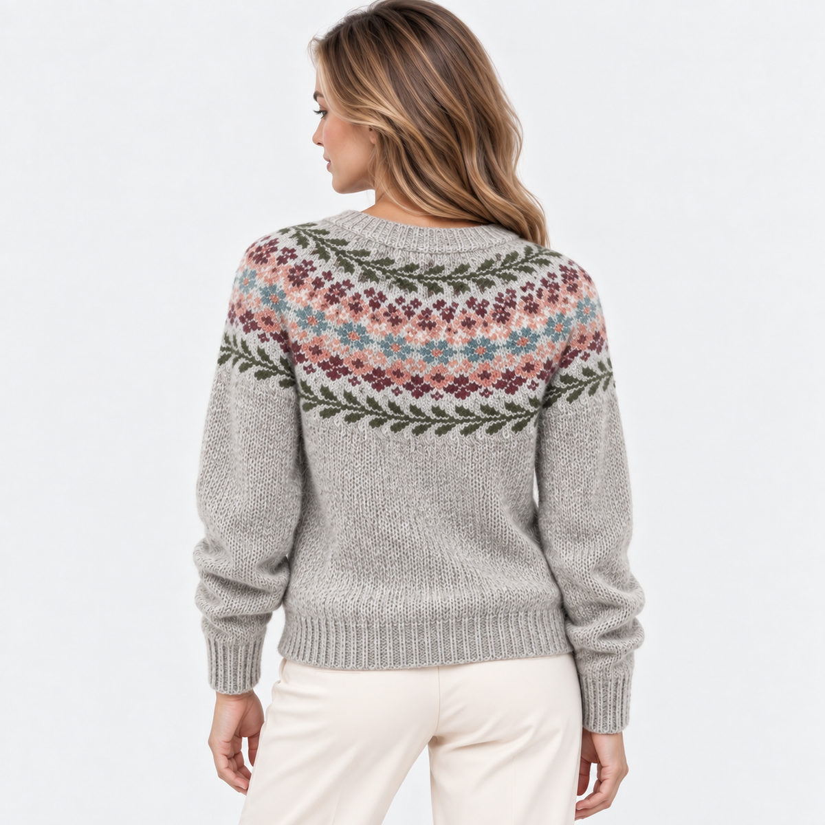 A woman shown from the back wearing a light gray knit sweater with a multicolor Fair Isle pattern across the shoulders and upper back, paired with cream pants, against a plain white studio background.