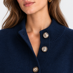 Close-up of a woman wearing a navy blue knit cardigan sweater with three large silver buttons on a white background.