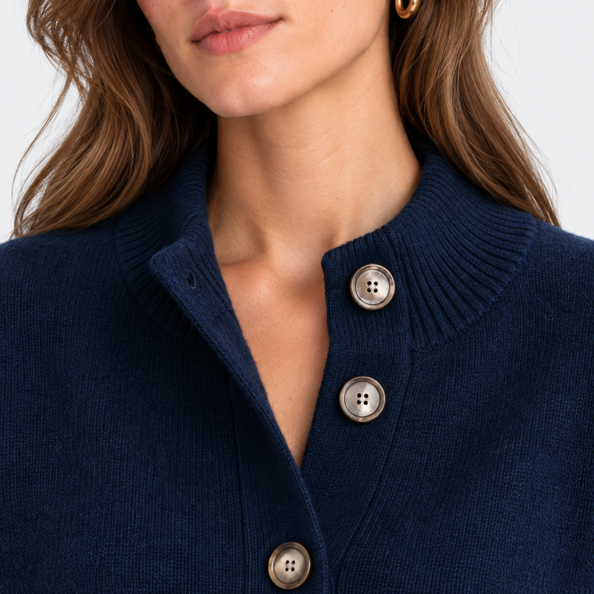 Close-up of a woman wearing a navy blue knit cardigan sweater with three large silver buttons on a white background.