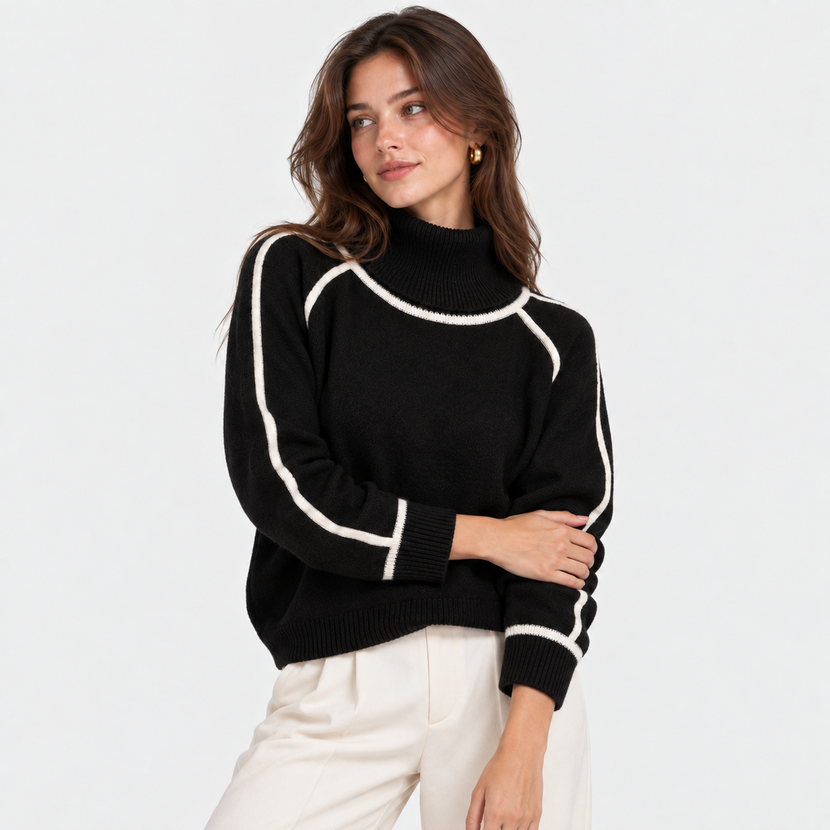 A woman wearing a black mock-neck knit sweater with contrasting white piping details on the shoulders and sleeves, paired with off-white trousers, against a plain white studio background.