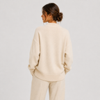 A woman shown from the back wearing a cream-colored knit sweater and matching knit pants against a light gray studio background.