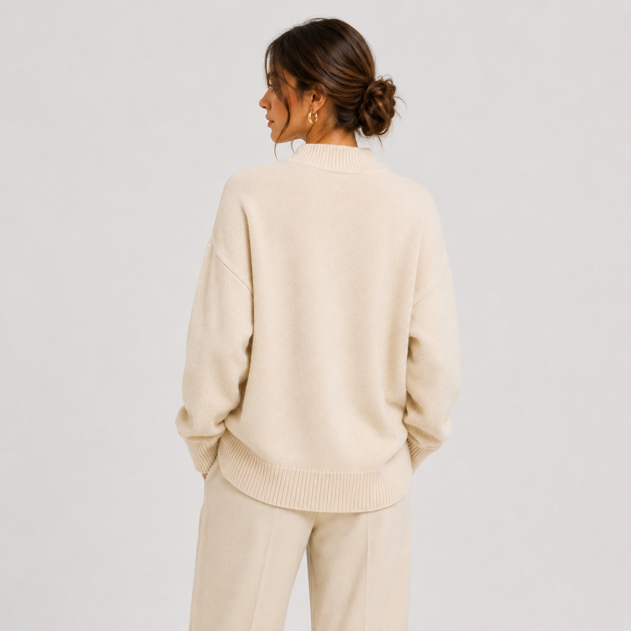 A woman shown from the back wearing a cream-colored knit sweater and matching knit pants against a light gray studio background.
