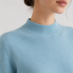Close-up of a person wearing a light blue ribbed knit sweater with a mock neck, showing the collar, shoulder, and lower face against a plain light background.