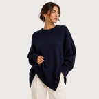 A woman wearing an oversized navy blue knit sweater and cream trousers, photographed against a clean light gray studio background.