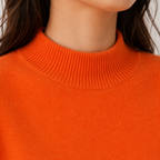 Close-up of a person wearing a bright orange ribbed knit sweater with a mock neck.