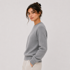 A woman wearing a light gray knit crewneck sweater and cream pants, photographed against a plain light gray studio background.