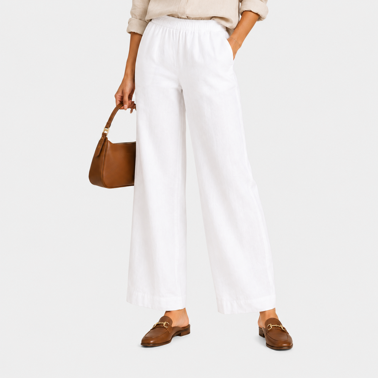 A model wearing white wide-leg cropped pants, styled with a beige top, brown leather loafers, and a brown handbag, set against a solid light gray background.