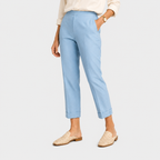 A model wearing light blue cropped trousers with rolled cuffs, paired with a cream blouse and beige woven mule flats, shown against a light gray studio background.
