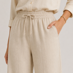 Close-up of a person wearing light beige linen drawstring trousers with a matching long-sleeve top, shown against a plain light background.