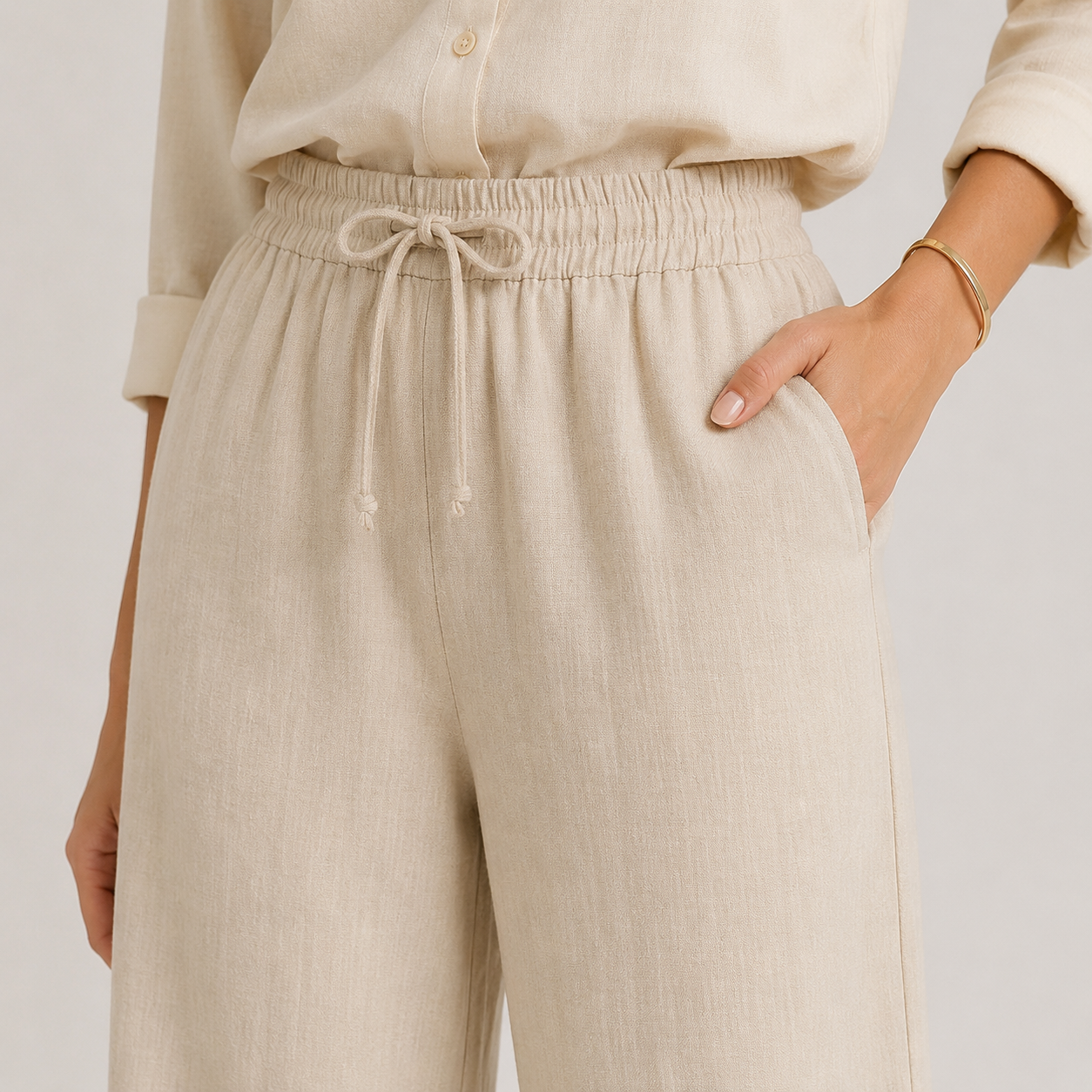 Close-up of a person wearing light beige linen drawstring trousers with a matching long-sleeve top, shown against a plain light background.