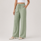 A model wearing sage green wide-leg pants with a drawstring waist, paired with a white crop top and beige pointed-toe heels, photographed against a neutral light gray studio background.