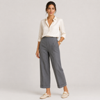 A woman modeling a white button-down shirt and gray cropped wide-leg trousers, paired with beige flat shoes, against a light gray studio background.
