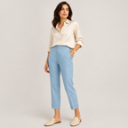 A woman modeling light blue cropped trousers with a cream button-down shirt and beige slip-on flats, standing against a light gray studio background.