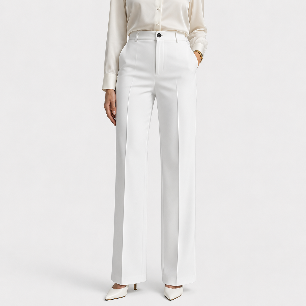 A model wearing high-waisted white wide-leg trousers, paired with a cream satin blouse and white pointed-toe heels, against a light gray studio background.
