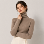 A woman wearing a taupe brown ribbed turtleneck sweater and a cream tie-waist skirt, posing against a neutral light gray background.