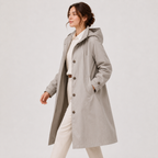 A woman wearing a light gray hooded coat over a cream outfit, photographed against a plain light gray studio background.