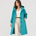 A woman modeling a teal hooded raincoat over a cream V-neck top and beige trousers, photographed against a light gray studio background.
