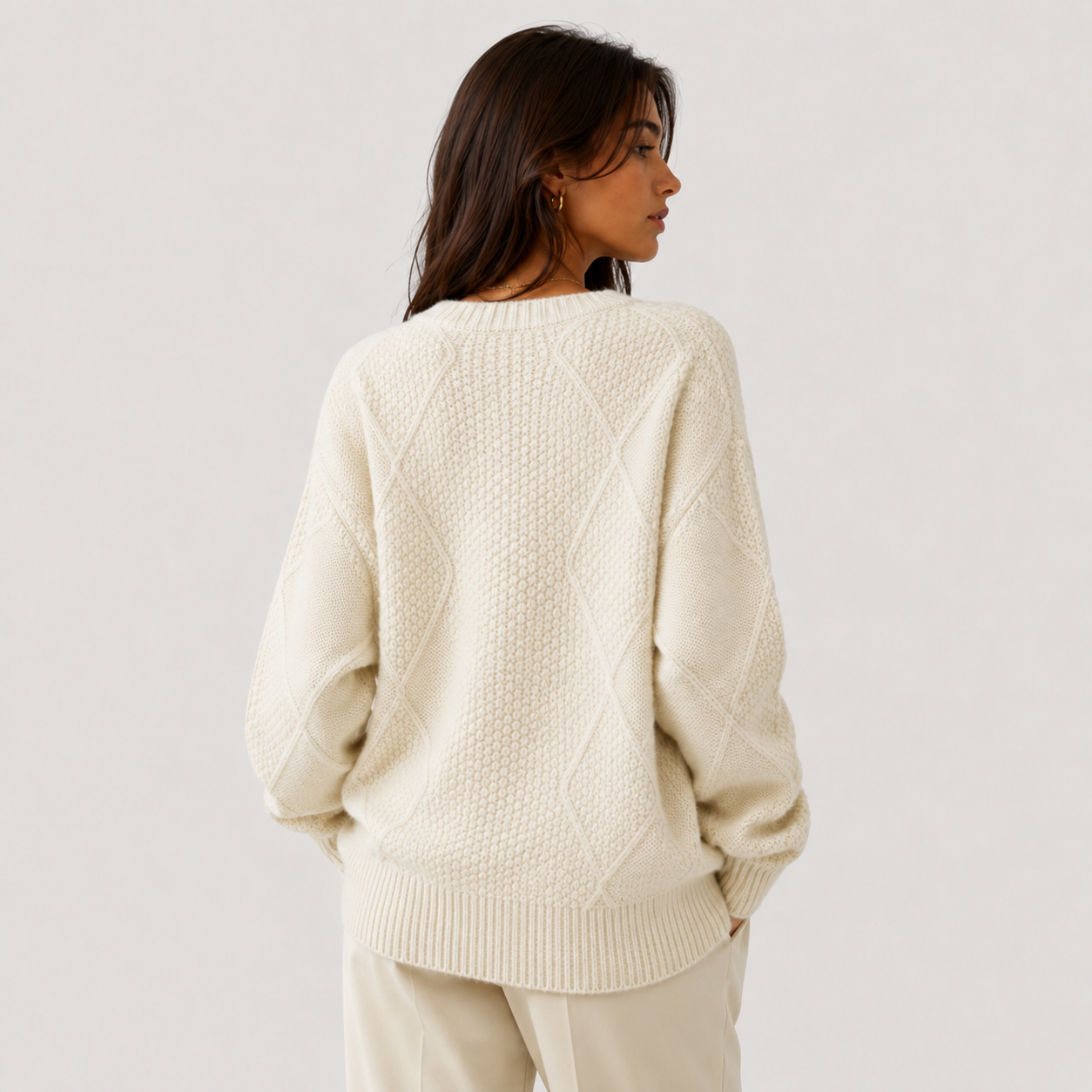 A woman shown from the back wearing a cream-colored, textured knit sweater and matching cream pants against a light gray studio background.