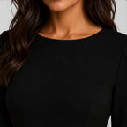 Close-up of a person wearing a black long-sleeve top against a neutral background