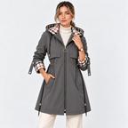 A woman models a dark gray hooded coat with a beige, brown, and black plaid lining on the hood and cuffs, paired with a white turtleneck and cream pants, against a light gray studio background.