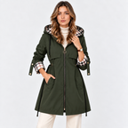 A woman models an olive green hooded parka jacket with a plaid-lined hood and cuffs, paired with a white turtleneck and cream pants, against a plain white studio background.