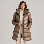 A woman models a mid-length, shiny taupe-brown hooded puffer jacket over a cream turtleneck and cream pants, set against a plain light gray studio background.