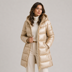 A woman wearing a shiny champagne-gold hooded puffer jacket over a cream turtleneck and cream trousers, standing against a light gray studio background.