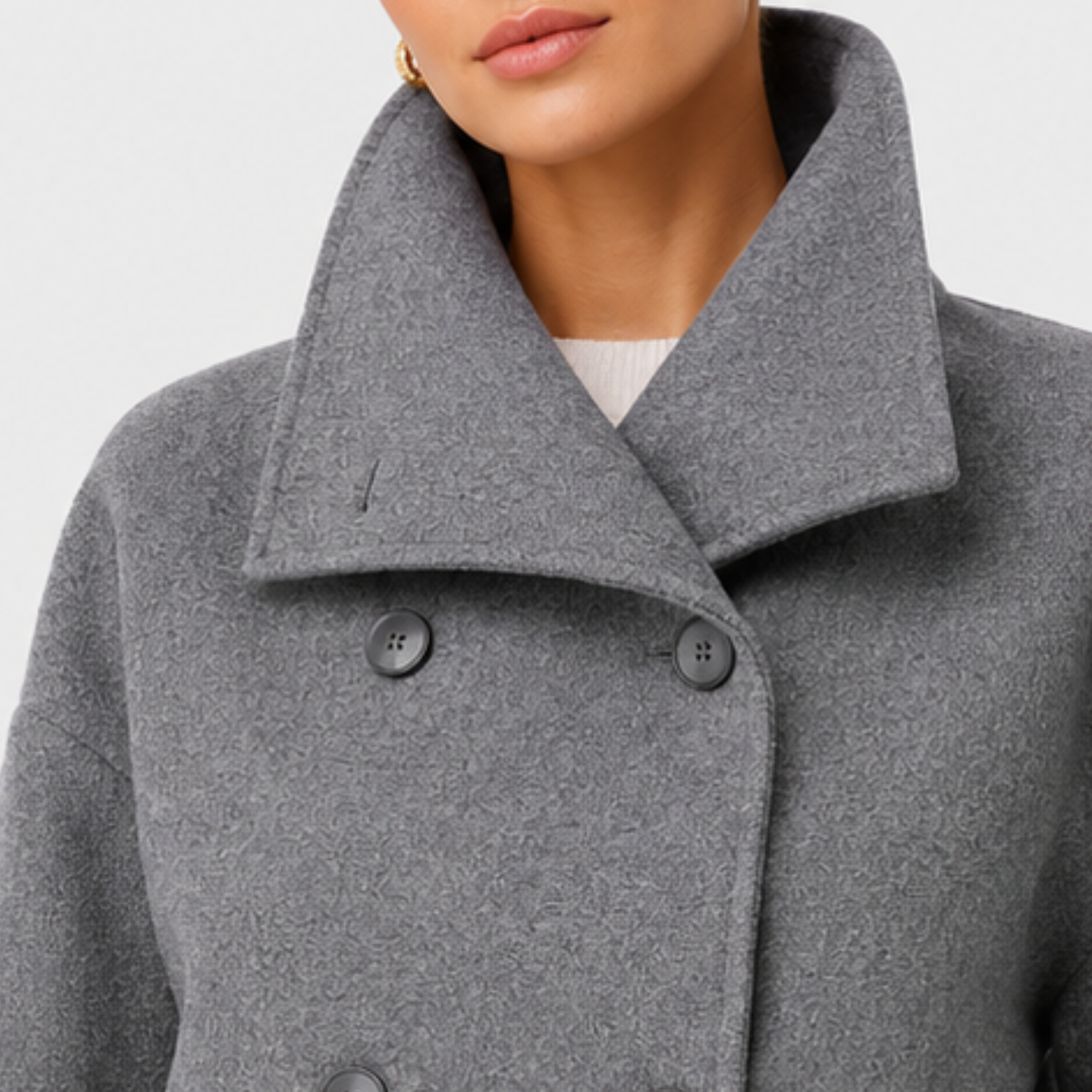 Close-up of a person wearing a gray double-breasted coat with a large folded collar and dark buttons, cropped from the lower face to the chest against a light neutral background.