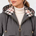 Close-up of a woman wearing a gray hooded jacket with a beige, black, and red plaid lining on the hood, styled over a cream ribbed turtleneck sweater.