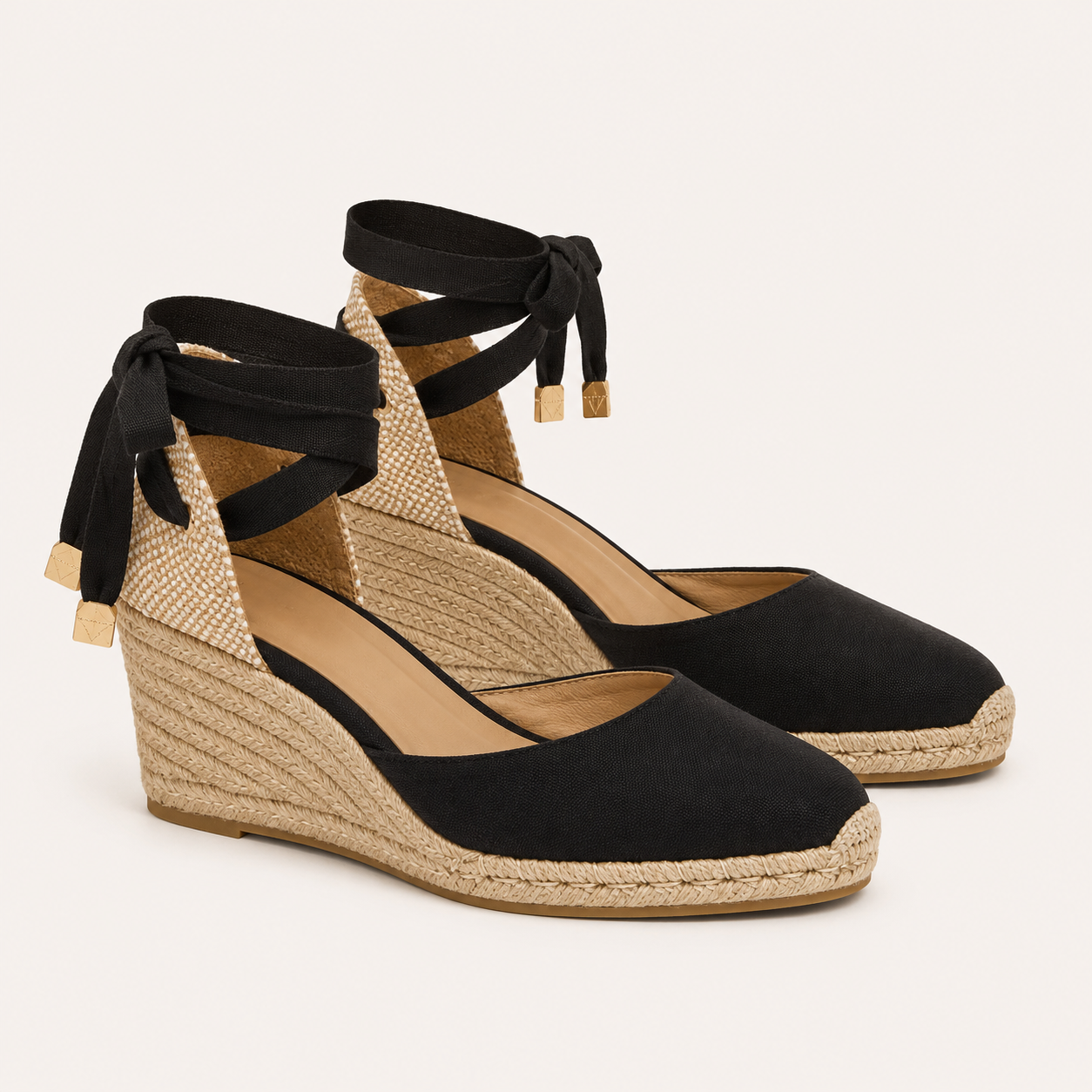 A pair of black wedge espadrilles with woven jute wedges, black ankle straps with bow details, and small gold-toned tips, shown on a light beige background.