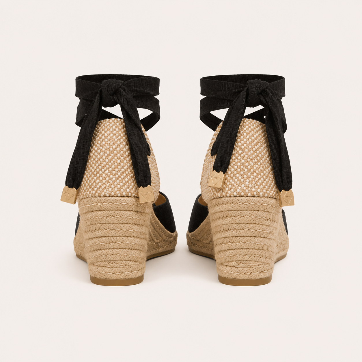 A pair of women's espadrille wedge sandals shown from the back, featuring a woven jute platform, black fabric wedge inserts, and black ribbon ankle straps tied in bows with small beige tags.