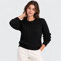 A woman modeling a black cable-knit crewneck sweater with cream pants, photographed against a clean light gray studio background.