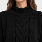 Close-up of a person wearing a black cable-knit mock neck sweater, showing the detailed knit texture and the lower edge of the hair against a plain light background.