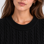 Close-up of a woman wearing a black cable-knit crewneck sweater, showing the ribbed collar and detailed knit texture.
