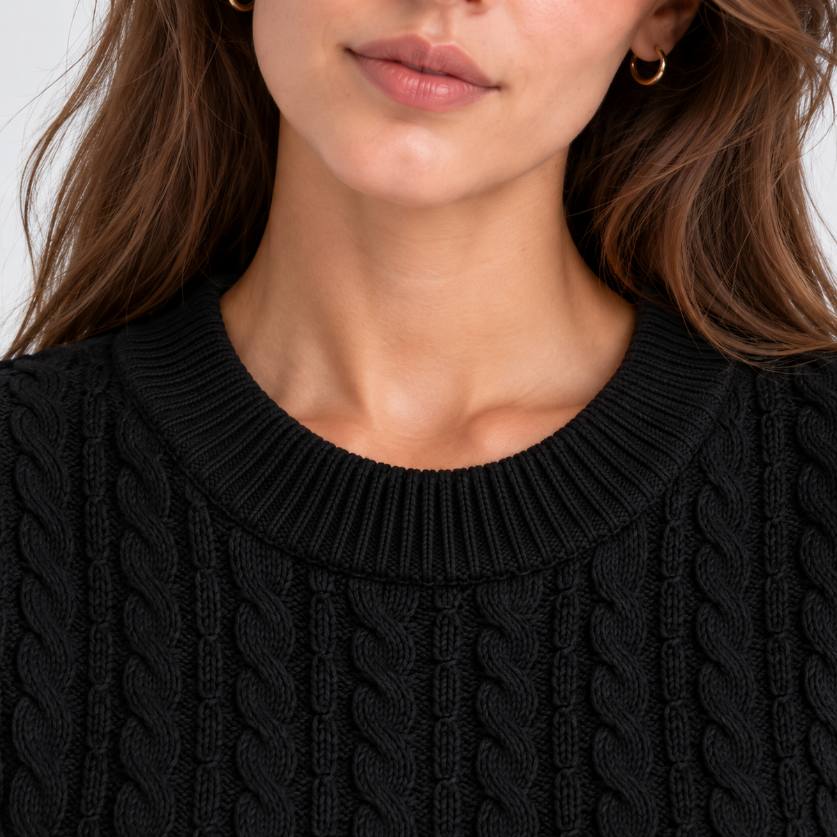 Close-up of a woman wearing a black cable-knit crewneck sweater, showing the ribbed collar and detailed knit texture.