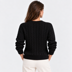 A woman viewed from the back wearing a black cable-knit sweater and off-white pants against a plain light gray studio background.