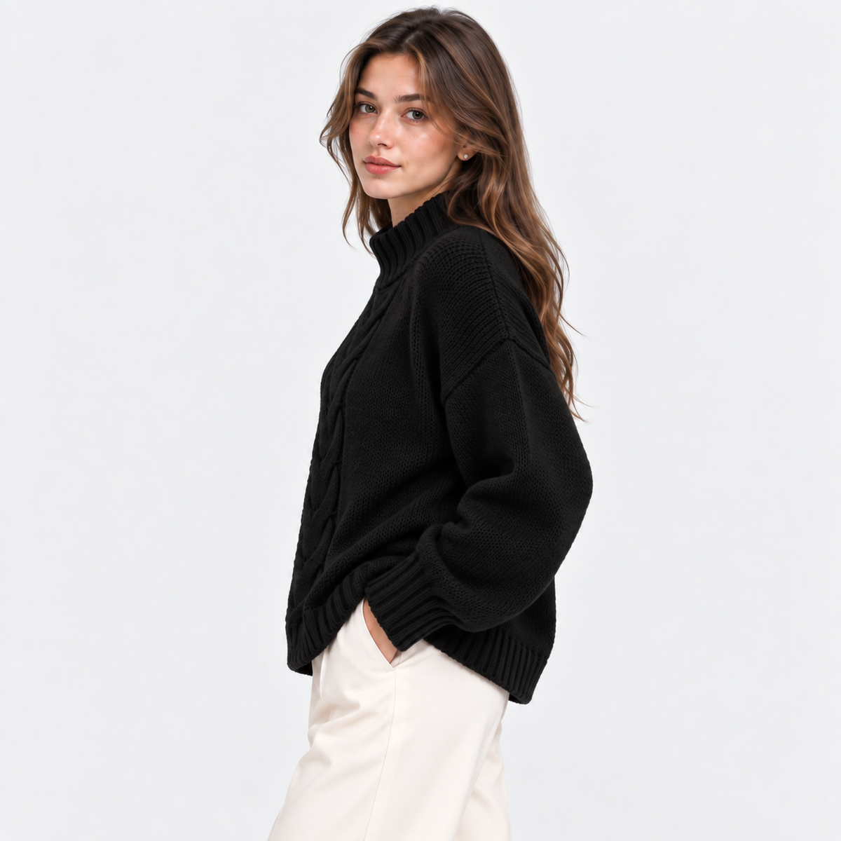 A woman wearing a black ribbed knit mock-neck sweater and cream-colored pants, photographed against a clean white studio background.