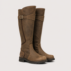 A pair of tall brown suede riding boots with a side buckle strap, shown against a light gray background.