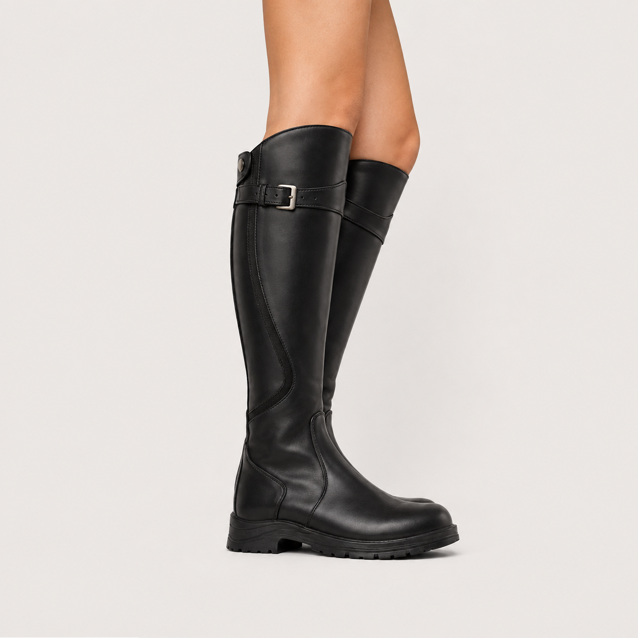 A pair of black knee-high leather boots with a buckle strap detail on the side, shown on a model's legs against a light gray studio background.