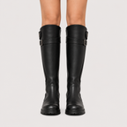 Black knee-high leather boots with buckle straps at the top, shown on a model's legs against a light gray background.