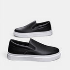 Black slip-on shoes with white soles on a light gray background